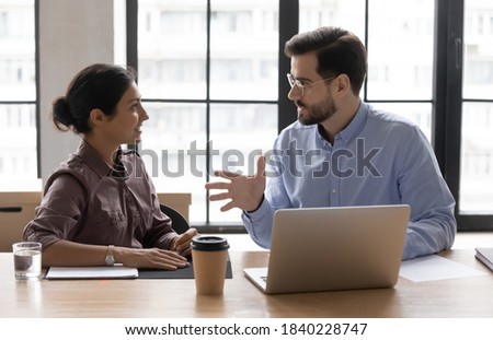 Multiracial diverse businesspeople talk work on laptop discuss business project at briefing in office. Multiethnic colleagues or partners brainstorm on computer at meeting. Collaboration concept.