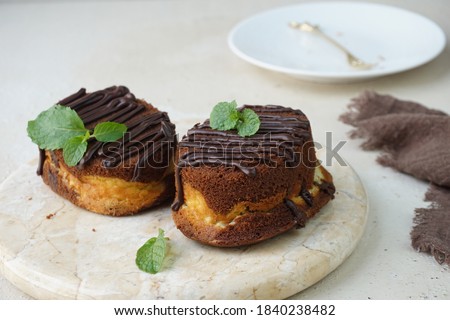 A picture focus on two chocolate cheese cake topped with chocolate glaze and mint leaves for garnish in marble board and grainy background