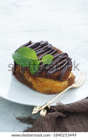 A close up picture of chocolate cheese cake in white plate and shiny background with chocolate glazing and mint leaves for food photography