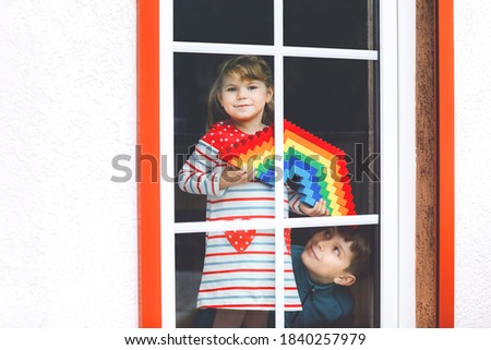Toddler girl and kid boy by window create rainbow with colorful plastic blocks during pandemic coronavirus quarantine. Two children, siblings made and paint rainbows around the world as sign.