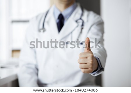 Unknown male doctor sitting with thumbs up sign at his working place in clinic, closeup. Perfect medical service in hospital. Medicine and healthcare concept