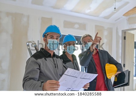 Professional meeting on a construction site between the architect and the craftsmen who wear a protective mask against covid-19 Royalty-Free Stock Photo #1840285588