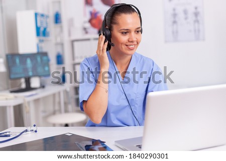 Medical staff talking with patient about prescription wearing headset with microphone in hospital office. Health care physician sitting at desk using computer in modern clinic looking at monitor. Royalty-Free Stock Photo #1840290301