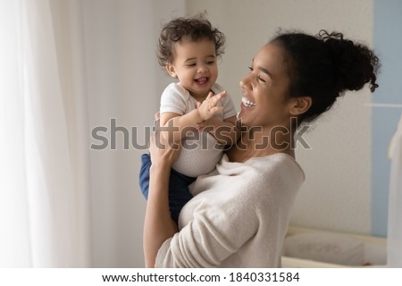 Smiling young african American mom hold in hands happy little ethnic baby infant play at home together. Happy biracial mother hug embrace feel playful with small toddler kid child show love care.