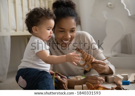 Happy young biracial mom lying on floor play with small curious ethnic baby infant at home. Smiling loving African American mother engaged in funny activity with small infant child. Childcare concept. Royalty-Free Stock Photo #1840331593