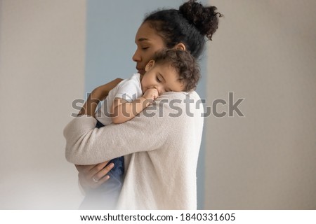 Loving young biracial mother hold in hands embrace small newborn baby child. Caring african American mom lean to chest hug cuddle little infant child, enjoy tender close family moment together. Royalty-Free Stock Photo #1840331605