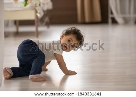 Portrait of cute little african American baby toddler crawl make first steps on home wooden floor. Small biracial newborn infant child learn walking play indoors. Childcare, upbringing concept. Royalty-Free Stock Photo #1840331641