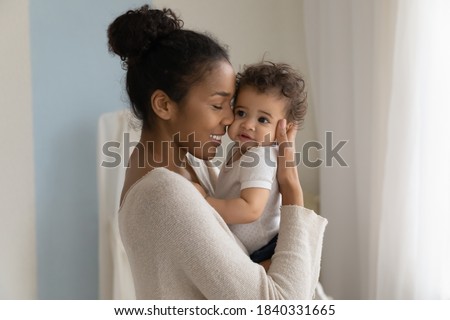 Happy young African American mom hold in hands hug cute little ethnic baby toddler show love care. Smiling biracial mother embrace cuddle small newborn infant child. Motherhood, childcare concept. Royalty-Free Stock Photo #1840331665