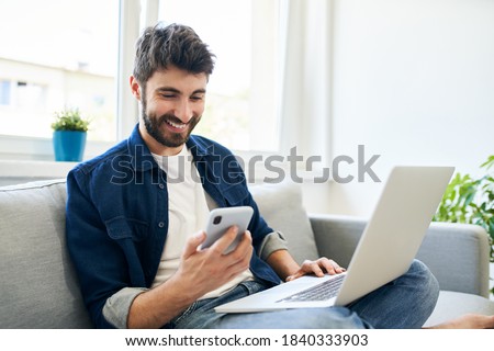 Young man working at home using laptop and smartphone Royalty-Free Stock Photo #1840333903