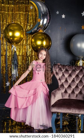 girl with long hair sits on a chair. Girl in a pink fluffy dress. Christmas photo session in the studio.