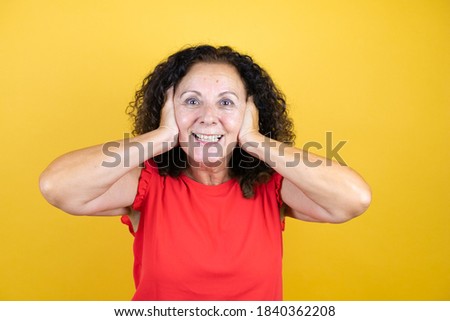 Middle age woman wearing casual shirt standing over isolated yellow background crazy and scared with hands on head, afraid and surprised of shock
