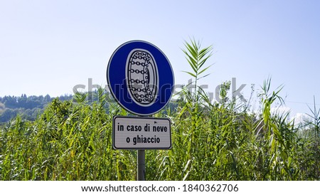 Road sign requiring drivers to have chains on their wheels in case of snow or ice ("in caso di neve o ghiaccio" in the italian language) on the asphalt (Pesaro, Italy, Europe)