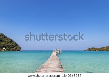 Old wooden bridge extended into the tropical seascape with beautiful blue sky.