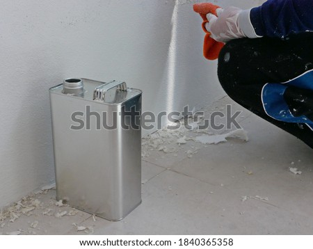 A gallon of thinner placed next to old concrete wall, while a painter is removing sticky rough glue and tape remain on the wall, as a preparation before starting the paint the house Royalty-Free Stock Photo #1840365358
