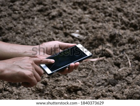male farmer holding smartphone with blank mock up touch screen over fertile arable soil ground