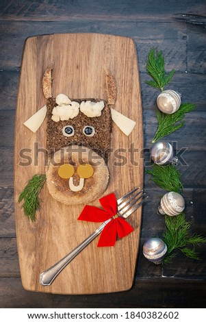 Funny food with edible symbol of 2021 bull cow made from bread, cheese and vegetables. Breakfast idea for kids. New Year Christmas food top view. Holiday, celebration, art food.