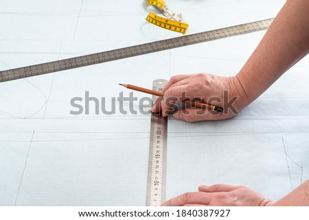 designer's hands with pencil and rulers on pattern layout of dress drawn on graph paper at home