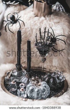 Happy Halloween. A skeleton's hand, black candles and spiders by the window, decoration for Halloween trick or treat party. Processed in black and white with film grained filter. Soft focus on hand