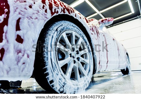 Washing red car with active foam at car wash service.