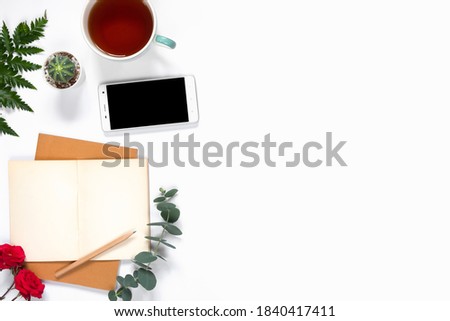 Top view of workspace with smartphone and notebook on white background