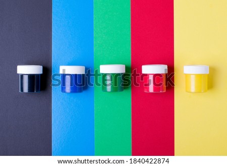 Multicolored gouache jars against the multicolored geometric background. Yellow, red, green, blue and black colors. Set for painting