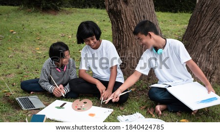 Three children sitting on green grass ground floor,painting color on canvas and talking,doing activity together with happy feeling,in a park