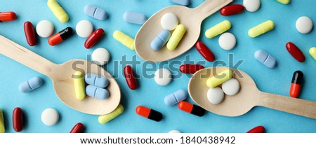 Colorful assorted pharmaceutical medicine capsules , tablets and pills in wooden spoon isolated on blue background. Dietary supplement healthcare product.Copy space for text.Banner