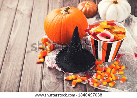 Halloween pumpkins, candies in bucket and black hat on wooden background