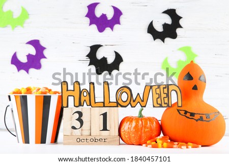 Word Halloween with candies in bucket, pumpkins and colorful bats on wooden background