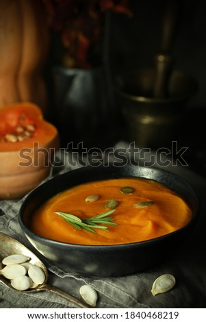 Thick pumpkin soup-puree with a sprig of rosemary on the background of pumpkin, seeds and autumn leaves