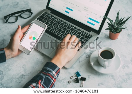 girl holding a mobile phone with one hand and typing on a laptop keyboard