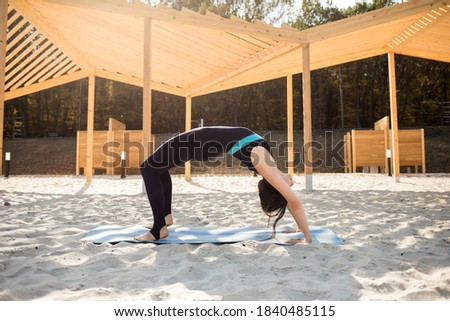 sportswoman in a tracksuit performs the exercise bridge on a blue Mat on a sandy beach