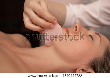 Young and beautiful woman during Chinese traditional massage - Gua Sha. Close-up photo. Beauty treatment in SPA salon. Anti-aging skin care