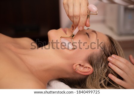 Young and beautiful woman during Chinese traditional massage - Gua Sha with stone roller. Close-up photo. Beauty treatment in SPA salon. Anti-aging skin care
