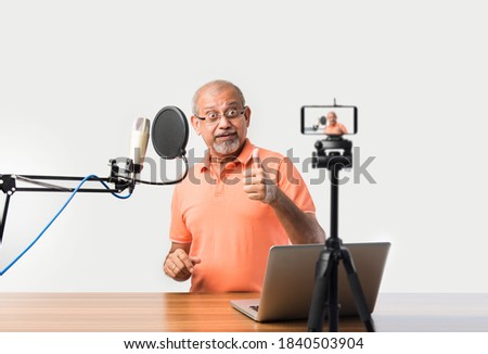 Confident Indian old man speaking in recording mic with filter while recording a video blog for his subscribers, looking at camera