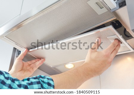Mans hands removing a filter from cooker hood for cleaning or service. Replacing filter in kitchen hood. Modern kitchen fan or range hood. Royalty-Free Stock Photo #1840509115