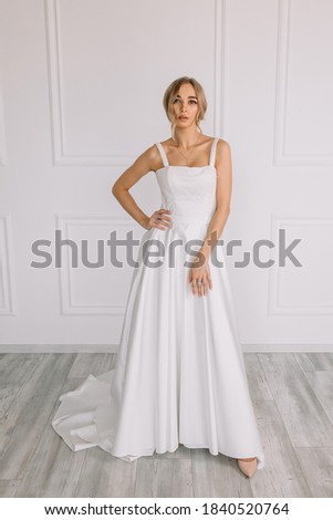 Young woman in a white wedding dress with long hair before the engagement ceremony on a white background with a model appearance important wife for the bride posing in front of the photographer	