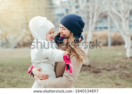 Happy smiling young Caucasian mother holding baby daughter outdoor on spring day. Family two people together outside at countryside or city. Authentic lifestyle with infant kids children. 