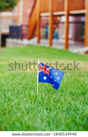 Australian flag standing on green grass in front of house. Australia day national holiday celebration. Nature background outdoor. Real estate property in Australia.