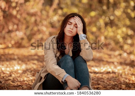 Tired or depressed young woman touching her head at autumn park. Millennial lady suffering from terrible headache, feeling lonely, stressed or unhappy, having problem Royalty-Free Stock Photo #1840536280