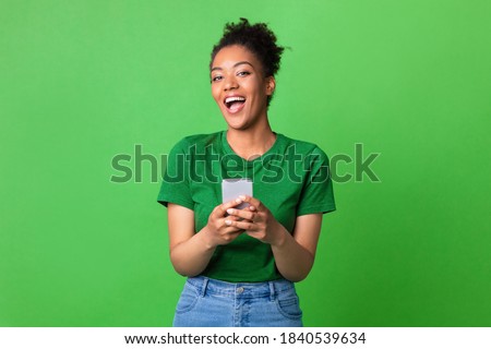Great Application Or Website. Portrait of excited african american woman using her mobile phone, isolated on green studio background, copy space. Positive black lady holding gadget, looking at camera