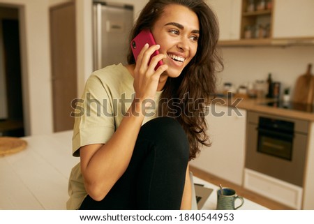 Technology and communication concept. Adorable Arabic girl with long dark hair smiling happily, calling best friend, sharing news. Cheerful young woman relaxing at home, speaking on mobile phone