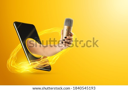 Hand holds a microphone through the smartphone screen on a yellow background. Concept for online concert, karaoke on the net, sound recording, stay at home