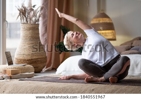 Mature Woman doing stretching yoga side bend at home. Royalty-Free Stock Photo #1840551967
