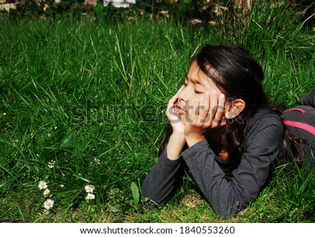 Image of a bored pre-teenage girl lying in the grass.