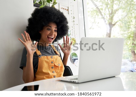 Happy excited hipster African American teen girl student with Afro hair using laptop computer video conference calling social distance friend in virtual chat, winning online sitting at table in cafe. Royalty-Free Stock Photo #1840561972