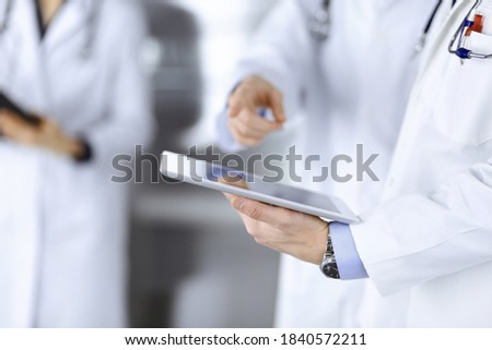 Group of unknown doctors use a computer tablet to check up some medical names records, while standing in a hospital office. Physicians ready to examine and help patients. Medical help, insurance in