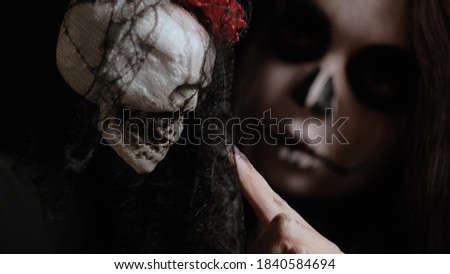 A girl with creepy make-up holds a white skull on a rope, runs her hand over it and lifts her veil. Conceptual symbol. Halloween attributes. October holiday.