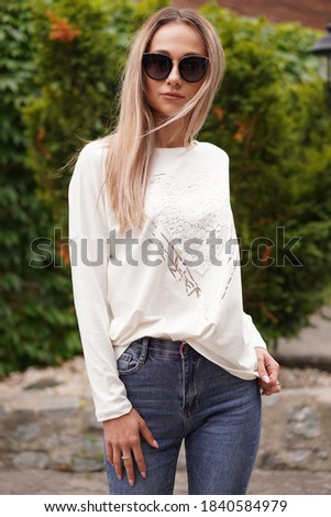 Young blond-haired fashion model takes photos for a fashion store outdoors with a blurred background.