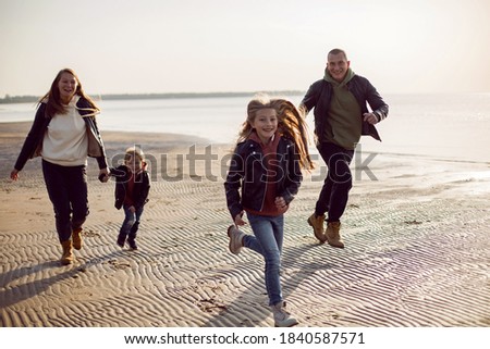 family in a leather jacket run along the beach with their dog in autumn